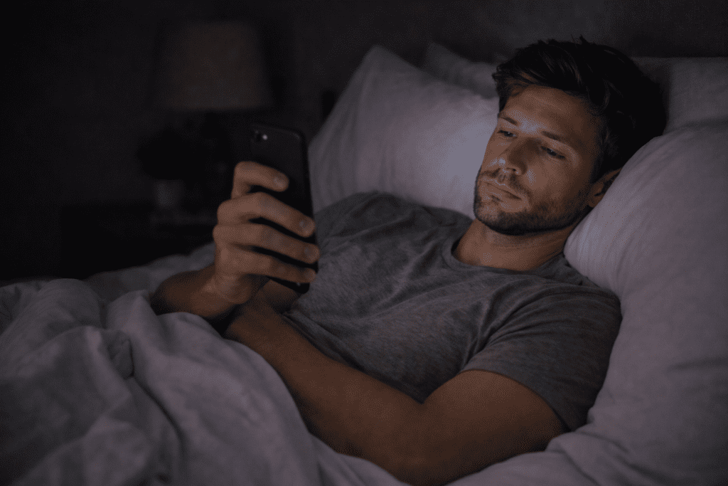 Man scrolling on his phone in bed at night, showing how screen time before sleep affects weight loss and fat loss after 30