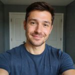 Smiling man in a casual blue shirt taking a selfie indoors with a bright, natural background.